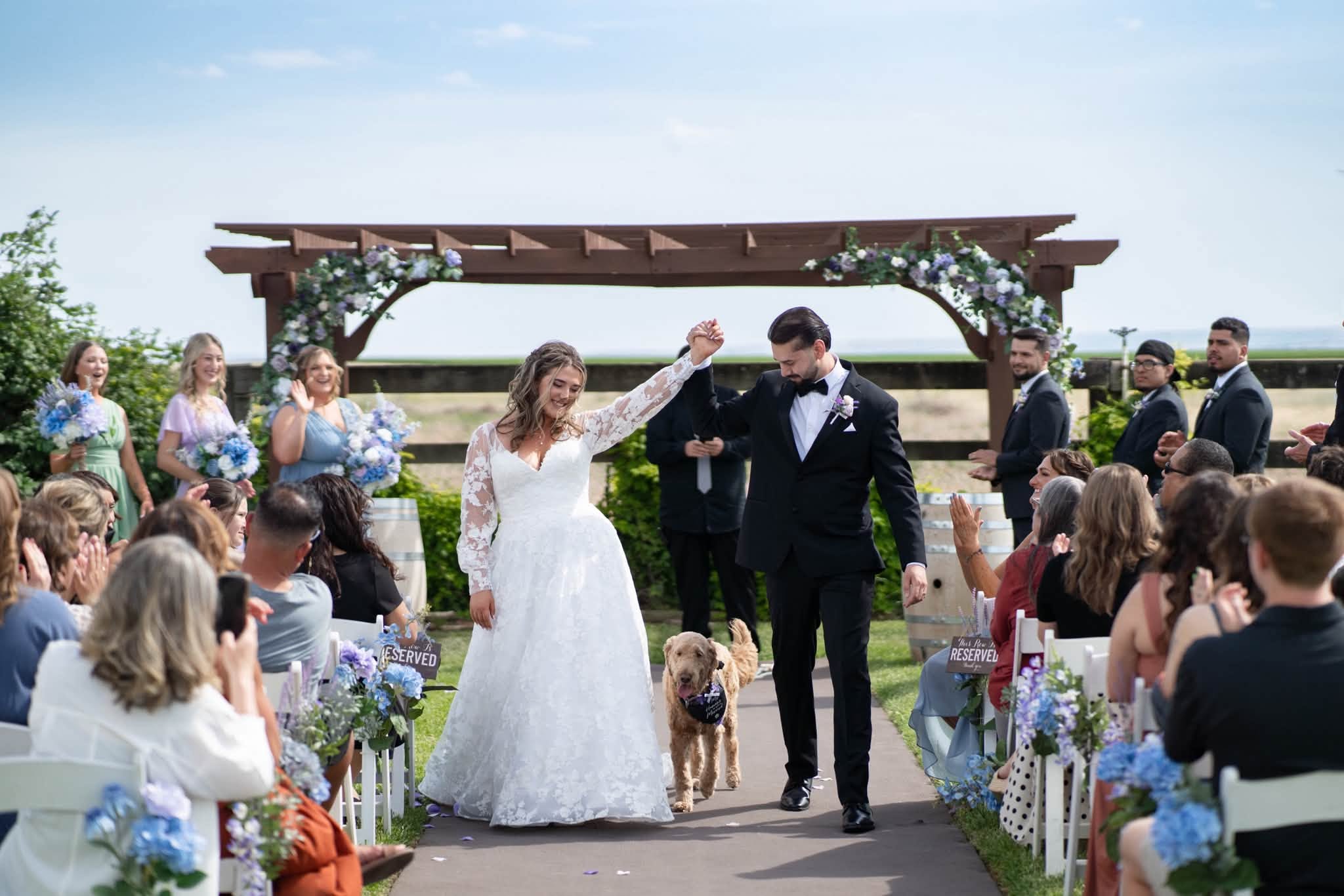 Newlyweds and their dog walking back up the outdoor ceremony aisle at Stone Ridge Estates